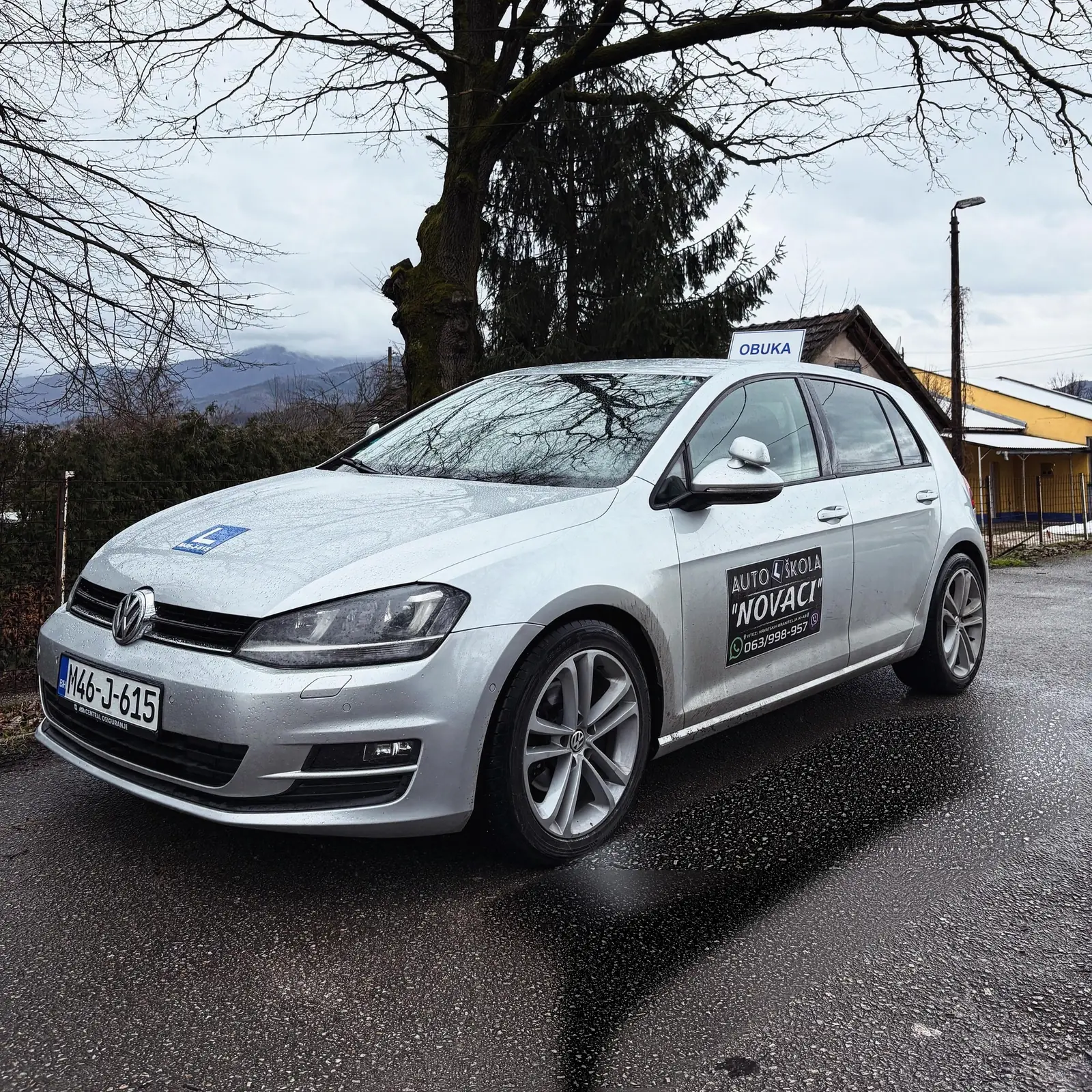 Srebrni Volkswagen Golf Autoškole Novaci s oznakom OBUKA na mokroj cesti u Vitezu
